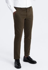 Chino marroni con una vestibilità dritta. Realizzati in un tessuto misto cotone, presentano tasche laterali e una superficie liscia. Abbinati a scarpe nere.