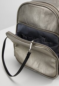 Metaliczny srebrny plecak z fakturowanym wykończeniem, wyposażony w komorę na zamek i czarny pasek. Wnętrze wyłożone jest ciemną tkaniną.