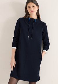 Robe à capuche bleu marine avec poignets blancs et cordons bleus. Tissu lisse, coupe décontractée, dotée de poches latérales et d'un détail de couture à l'avant.
