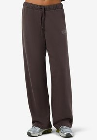 Ruske trenirke med smučnim pasom, širokimi hlačnicami in diskretnim logotipom; narejene iz mehke, teksturirane tkanine.