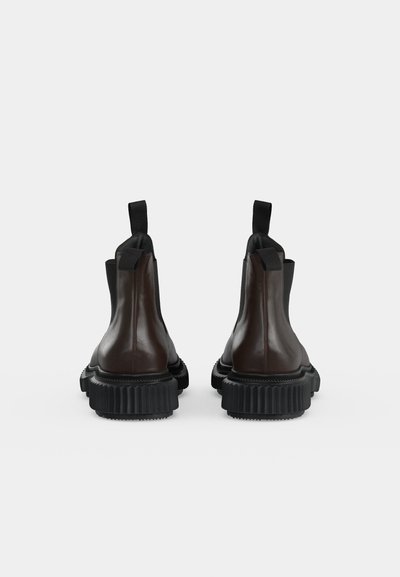 Paire de bottines Chelsea en cuir marron foncé avec semelles épaisses noires rainurées vue de dos sur fond blanc.