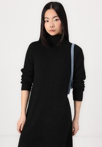 Black knitted dress with a high turtleneck and long sleeves. Features a denim strap on the left shoulder, creating a mixed-material design.