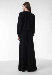 Zwarte gebreide trui en wijde broek, met een zachte textuur en een relaxte pasvorm. Het ontwerp heeft licht verlengde schouders en een lage hals.