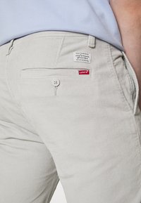 Ljusgrå kordflortbyxor med framficka med knappstängning och en liten röd Levi's etikett på bakfickan.