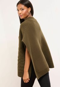 Pletený pončo olivovo zelenej farby s textúrovaným vzorom káblov na jednej strane, so širokými rukávmi a vysokým výstrihom.