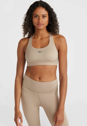 Beige sportbeha met een scoop hals, brede bandjes en een logo in het midden. Gecombineerd met hoge beige leggings met een gladde textuur.