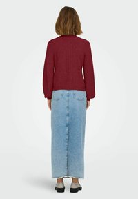 Bordeaux gebreide trui met een geweven patroon, gedragen met een lichtblauwe denim maxi rok met een rafelige zoom. Gecombineerd met grijze schoenen.