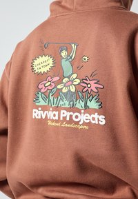 Smeđa majica s grafikom u boji golfera i cvijeća. Natpis glasi "Rivvia Projects Weekend Landscapers," s dodatkom balončića za govor.