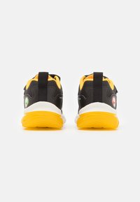Zwarte sportieve schoenen met gele accenten en witte zolen. Kenmerken zijn een gestructureerde bovenkant, hiel lussen en logodetails aan de zijkanten.