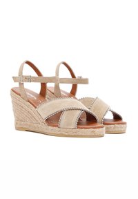 Beige suède wedge sandalen met een touwzool, open teen en kruislings ontwerp, versierd met zilveren kraalaccenten langs de randen.