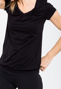 Top negro de manga corta con escote en V y detalle fruncido en el cuello. Fabricado en una tela suave y elástica, tiene un dobladillo fruncido para un aspecto ajustado.