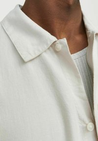 Witte linnen blouse met een klassieke kraag en een enkele knoopsluiting bij de halslijn, met een subtiel gestructureerd patroon eronder.