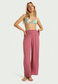 Lyserøde vide bukser med smocket talje, parret med en blomstermønstret bralette i nuancer af grønt og pink.