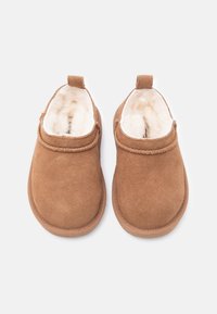 Ζευγάρι καφέ σουέντ παντόφλες με λευκή χνουδωτή επένδυση, στρογγυλεμένα δάχτυλα και θηλιές πίσω, τοποθετημένες σε λευκό φόντο.