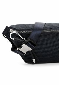 Bolsa de tela negra texturizada con un cierre y accesorios plateados, que cuenta con una correa negra y un clip para un cierre seguro. Diseño delgado y compacto.