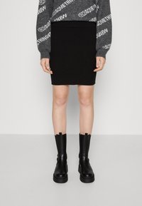 Svart ribbad stickad kjol med hög midja, kombinerad med kraftiga svarta platåstövlar. Överdelen har en grå och vit mönstrad tröja.