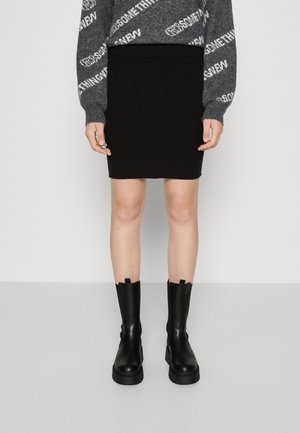 Falda negra de punto canalé con una cintura alta, combinada con botas de plataforma negras y gruesas. La parte superior presenta un suéter de patrón gris y blanco.