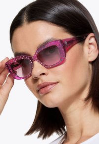 Occhiali da sole rosa con una montatura geometrica, decorati con piccoli chiodi multicolori lungo il bordo superiore, dotati di lenti sfumate e stanghette spesse.