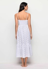 Rochie lungă albă, fără mâneci, cu un model din ochiuri, bust smocked și fustă în straturi. Material ușor, cu o siluetă fluidă.