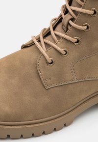 Bota de ante marrón claro con punta redonda, cordones beige, ojales de metal y suela de goma texturizada con un profundo diseño para mayor tracción.