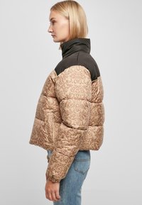 Puffjakke med en beige mønstret nedre del og en svart øvre del. Har høy krage og elastiske mansjetter for en best mulig passform.