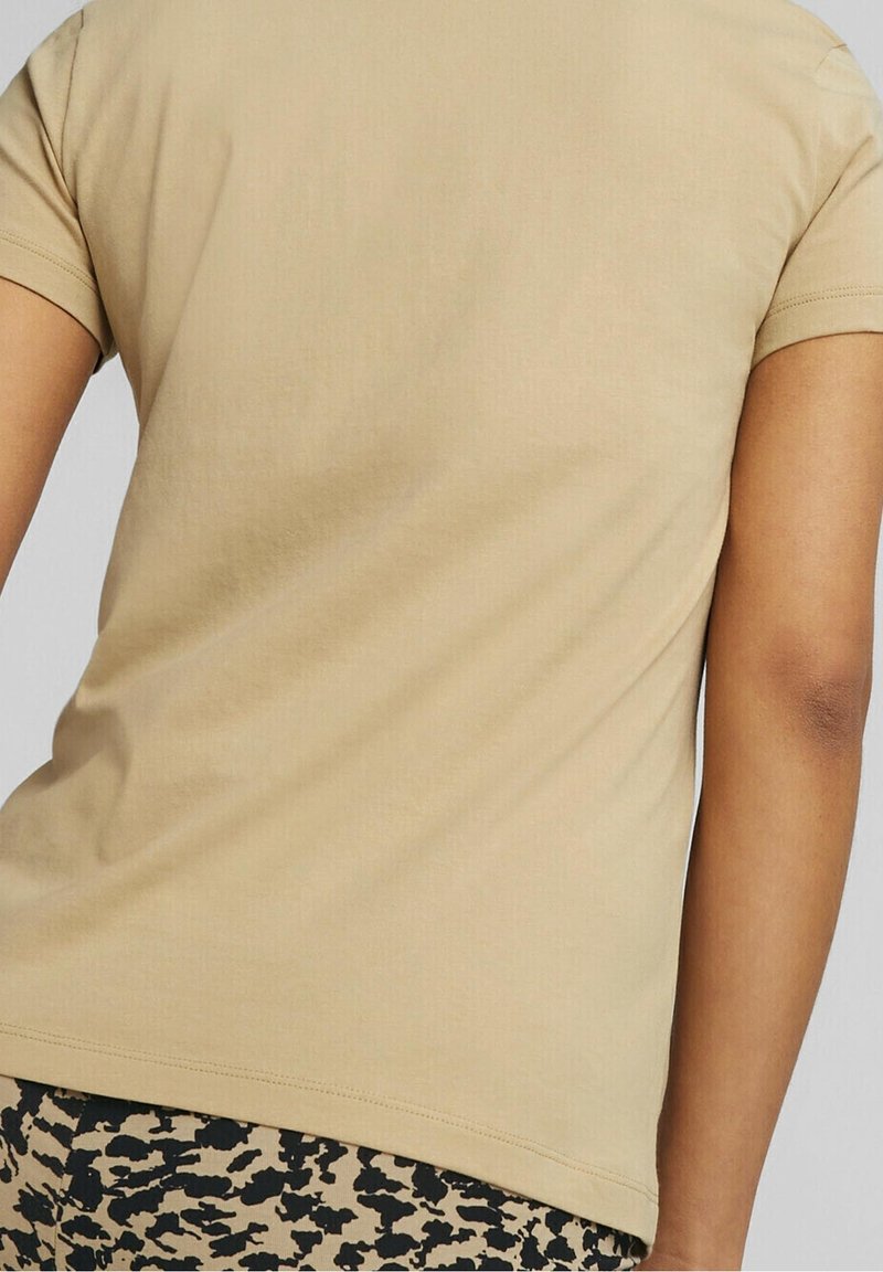 Beige fitted t-shirt with short sleeves, smooth cotton texture, rounded neckline, and a plain back, paired with black and beige patterned leggings.