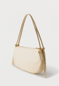 Μπεζ τσάντα σε σχήμα ημισελήνου με διπλούς ρυθμιζόμενους ιμάντες ώμου και χρυσές αγκράφες σε λευκό φόντο.