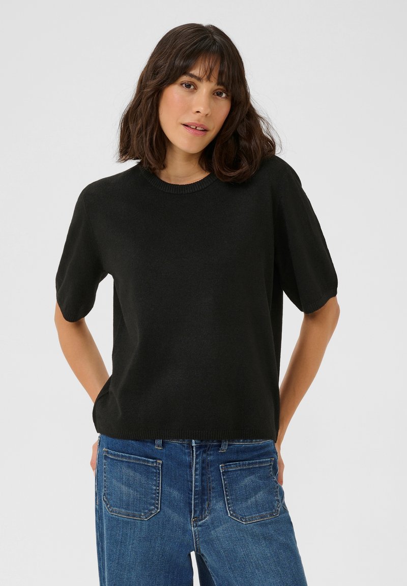 Maglione nero a maniche corte con collo rotondo, realizzato in un tessuto morbido, abbinato a jeans blu con tasche posteriori e cuciture visibili.