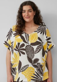 Witte blouse met korte mouwen en een V-hals, versierd met een gedurfde blaadjesprint in geel en bruin. Gemaakt van lichtgewicht stof, heeft het een ontspannen pasvorm.
