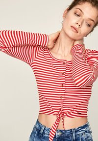 Camisetta cropped a righe rosse e bianche con maniche lunghe, chiusura a bottoni davanti e dettaglio della vita annodato. Tessuto a coste testurizzato.