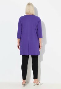 Lila Tunika mit drei Viertelärmeln, kombiniert mit schwarzen Leggings und silbernen Absatzsandalen, die ein einfaches und entspanntes Design zeigen.