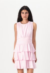 Ærmeløs rosa kjole med struktureret overflade, som har et tætsiddende skørt og tiered ruffle nederdel. Simple rund halsudskæring og elastisk talje.