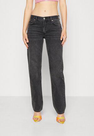 Black denim jeans with a straight leg fit, featuring five pockets and a front button closure. Worn with colorful heeled sandals.