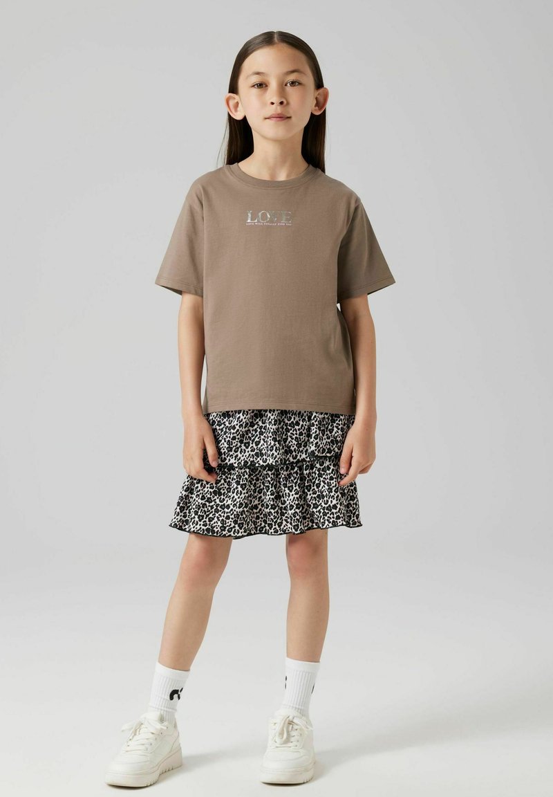 Brun bomullströja med texten "LOVE", lager av svart och vit leopardmönstrad kjol, samt vita sneakers med ribbade vita strumpor.