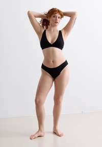 Schwarzes Bikini-Set mit einem dreieckigen Bralette und dünnen Trägern sowie tief geschnittenen Slips. Glattes, elastisches Material mit minimalen Nähten.