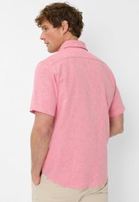 Camicia a maniche corte con bottoni in tessuto rosa chiaro con una trama sottile, caratterizzata da un colletto standard e un orlo curvo.