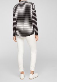 Musta-valkoinen raidallinen pitkähiha paita, jossa on pyöreä pääntie, yhdistettynä slim fit -valkoisiin farkkuihin ja valkoisiin lenkkareihin. Rentoa istuvuutta ja yksinkertaista muotoilua.