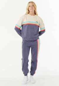 Zweiteiliges Set bestehend aus einem cremefarbenen und blauen Sweatshirt mit horizontalen, mehrfarbigen Streifen und passenden blauen Jogginghosen mit seitlichen Akzenten.