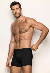 Boxeri negri dintr-un material moale, cu o croială ajustată, talie elastică și o textură netedă. Modelul stă cu o mână ajustând talia.