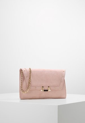Zachte roze suède clutch met gouden kettingriem, gouden studs langs de randen en een gouden en zwarte decoratieve sluiting op een witte ondergrond.