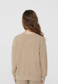 Jasnobrązowy, oversize'owy sweatshirt z opuszczonymi ramionami i okrągłym dekoltem. Miękka tekstura, minimalne wykończenia i ściągacze przy rękawach.