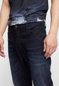 Mörka denimjeans med slim fit, med ett subtilt randmönster, femfickdesign och metallknappdetalj i midjan.