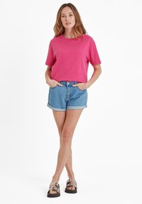 Pink cotton T-shirt paired with blue denim shorts, featuring rolled hems. Worn with black sandals having silver buckles. Plain background.