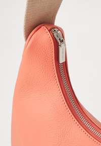 Borsa in pelle corallo con superficie testurizzata, dotata di una cerniera in argento e una tracolla in tessuto. La cerniera è parzialmente aperta, rivelando la fodera interna.