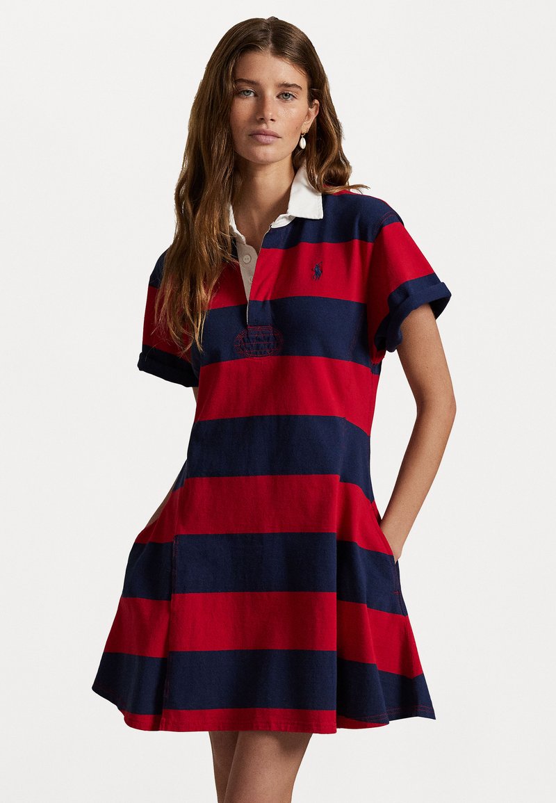 Rugby-stijl jurk met gedurfde marineblauwe en rode horizontale strepen, een witte polokraag, korte opgerolde mouwen en zijzakken.