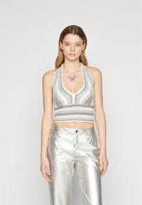 Halterneck crop top i lyseblå og gråstripet strikk med åpenarbeid detaljer, sammen med sølvmetallic vide bukser.