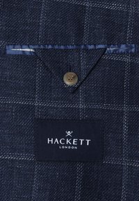 Tmavomodrá vzorovaná látka s vreckom so zapínaním na gombík a čiernou štítkom s bielym nápisom "Hackett London".