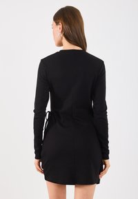 Musta pika varrukaga kleit, millel on lähedane siluett, külje sidumisdetail ja sile tekstuur. Kujundus sisaldab minimalistlikku stiili ringikujulise kaelusega.