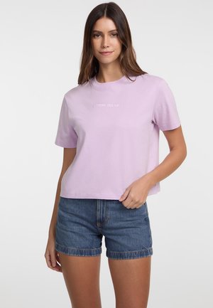 Gaiši violets īsais T-krekls, izgatavots no kokvilnas, ar īsām piedurknēm un izšūtu "GUESS JEANS" logo baltā krāsā. Kombinēts ar džinsiem šortiem.