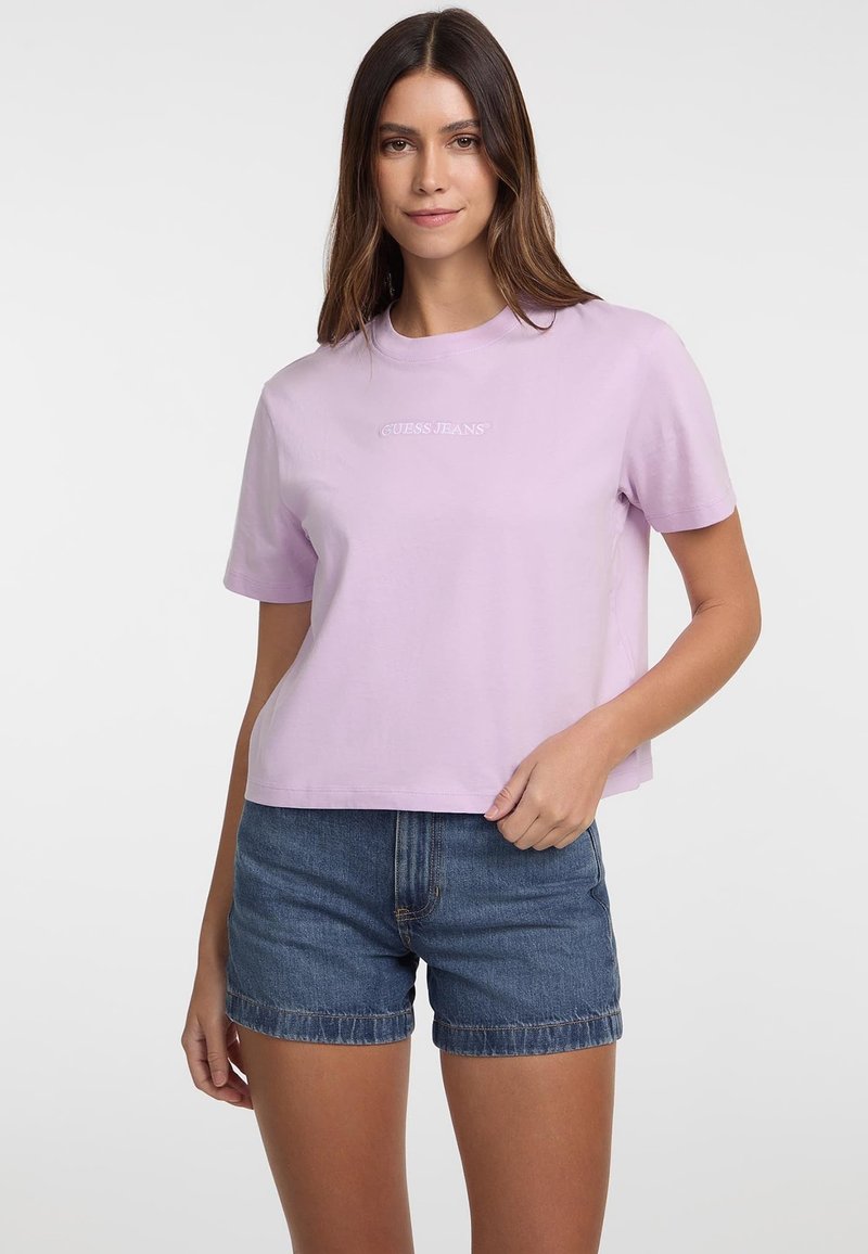 Gaiši violets īsais T-krekls, izgatavots no kokvilnas, ar īsām piedurknēm un izšūtu "GUESS JEANS" logo baltā krāsā. Kombinēts ar džinsiem šortiem.